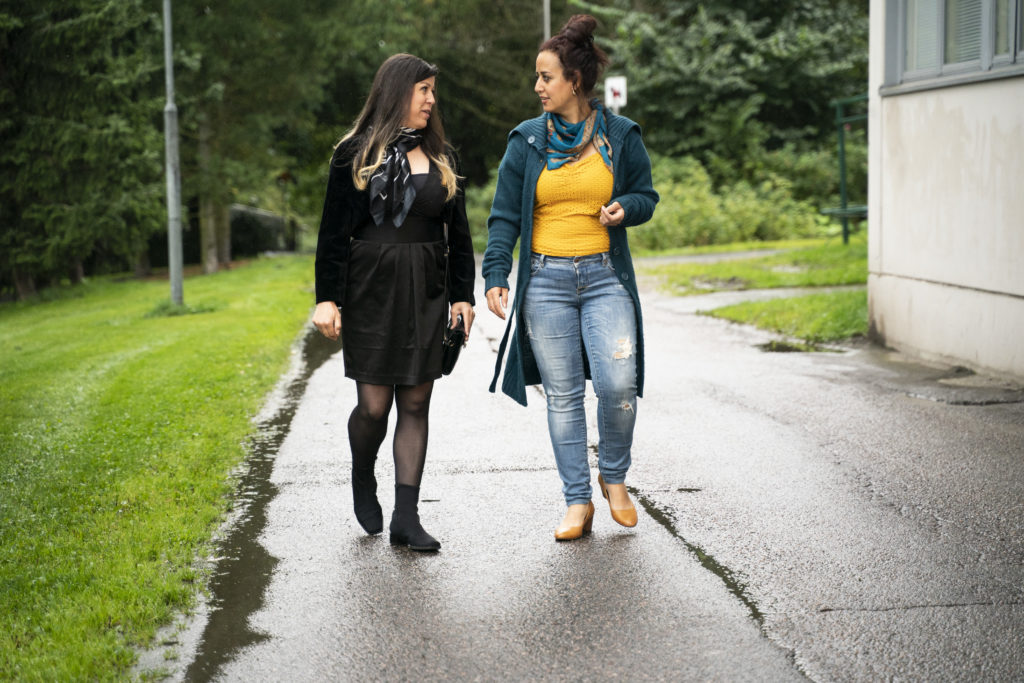 Amal Abofakher ja Fardoos Helal. Kaksi naista kävelevät sateesta märällä asfalttitiellä, toistensa kanssa keskustellen.