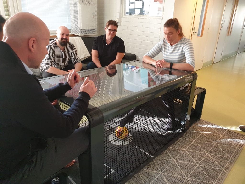 Mira Paakko ja Jarmo Lonkola pelaavat Subseccer pöytäjalkapallopeliä Jarno Saarisen ja Markus Toivasen seuratessa vierestä sohvalla.