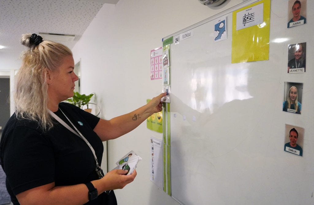 Jeannette Auvinen asettaa päiväohjelmakuvia valkotaululle.