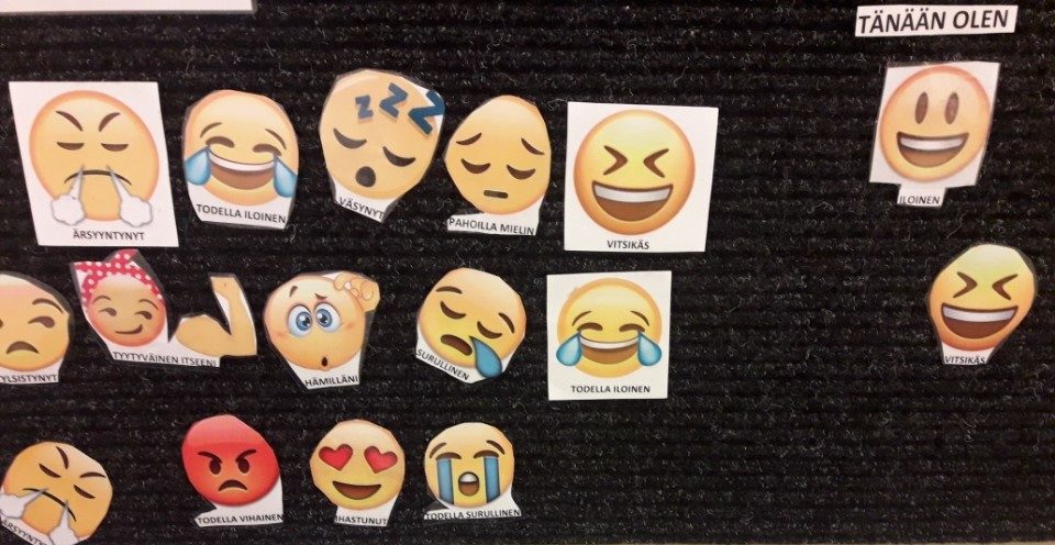 Mustalla tarraseinällä useita erilaisia keltaisia emoji-kuvia.