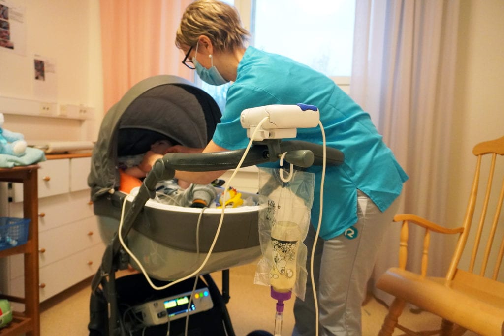 Työntekijä on kurottautunut lastenvaunujen ylle laittamaan hattua vauvan päähän.