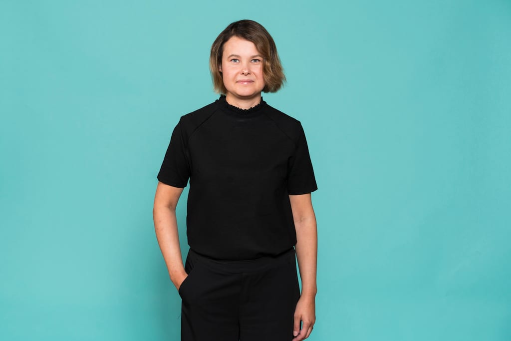 Anna Eskola seisoo turkoosin seinän edustalla.