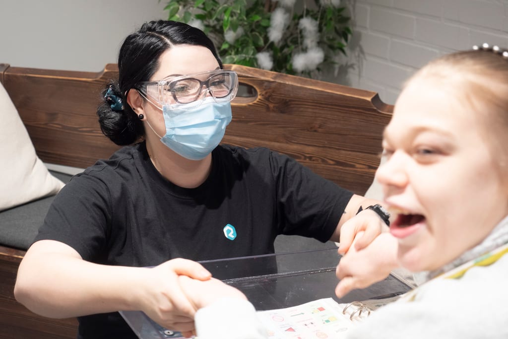 Minttu Eronen pitää kiinni käsistä tyttöä, joka istuu pyörätuolissa.