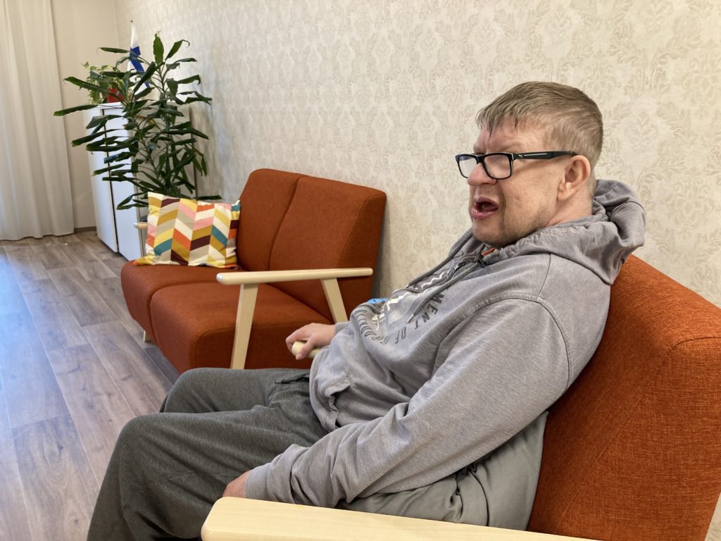 Mies istuu punaisella sohvalla.