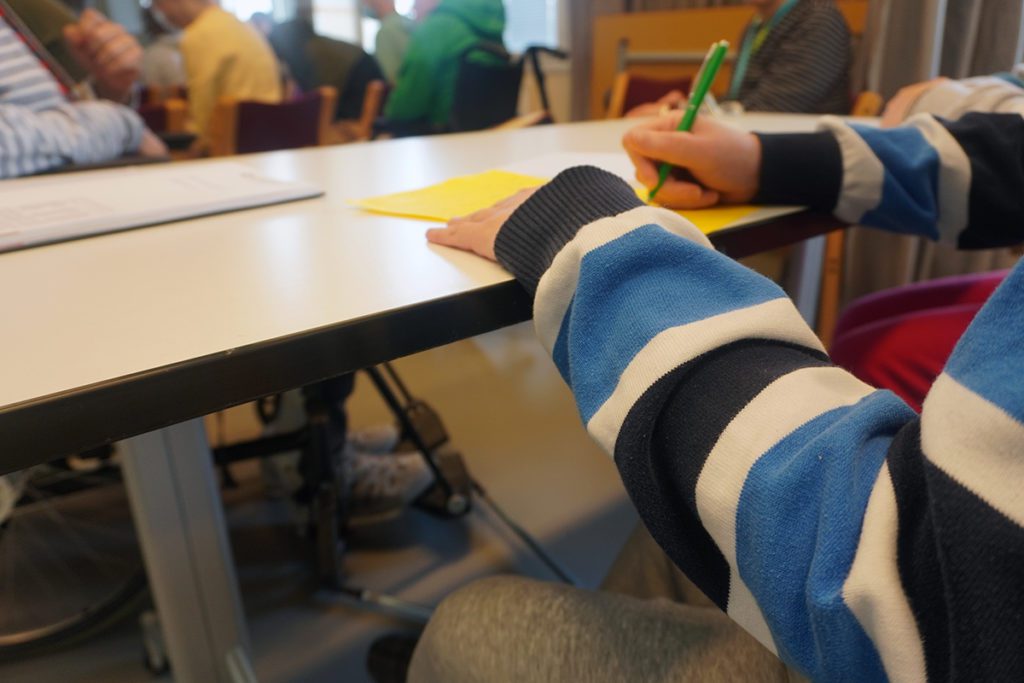 Henkilö tekee muistiinpanoja keltaiselle paperille pöydän äärellä.