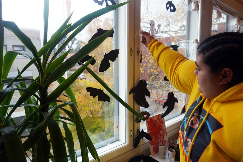 Nainen ripustaa halloween koristetta ikkunan eteen.